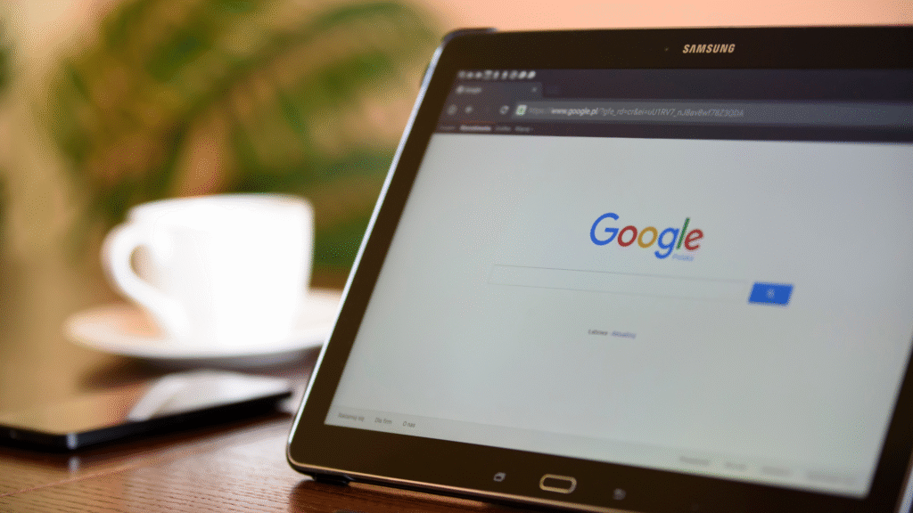 A desk with laptop opened on Google homepage, with a cup of coffee in the background.